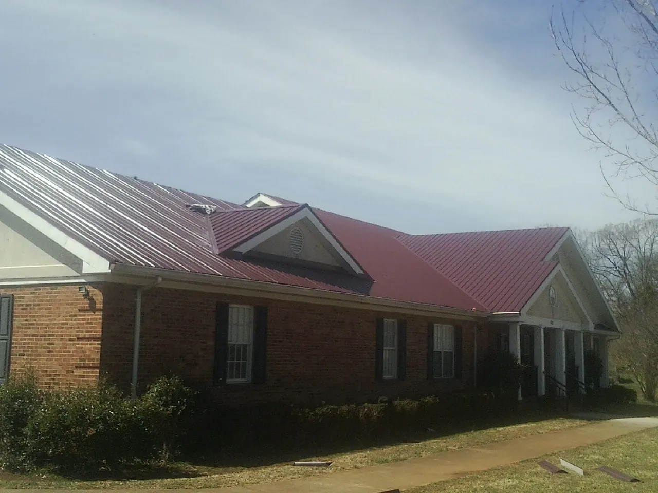 Red metal roof with gabled entries on a long brick building, from a Hail Damage Roof Repair job in Utica
