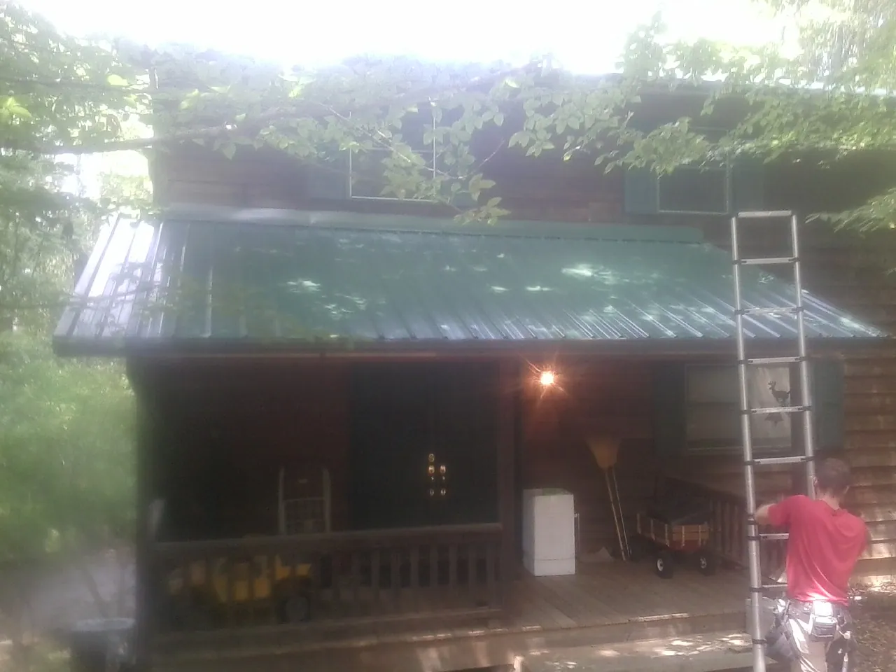 Worker on a ladder at the green porch roof of a wooded cabin in Utica